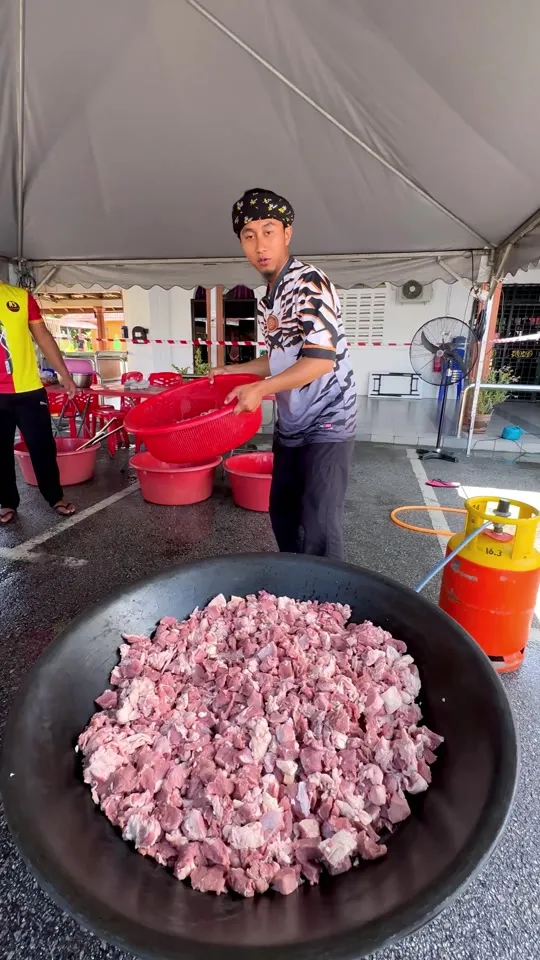 Abe Wea di bawah khemah, di belakang kawah besar berisi daging mentah yang dipotong dadu