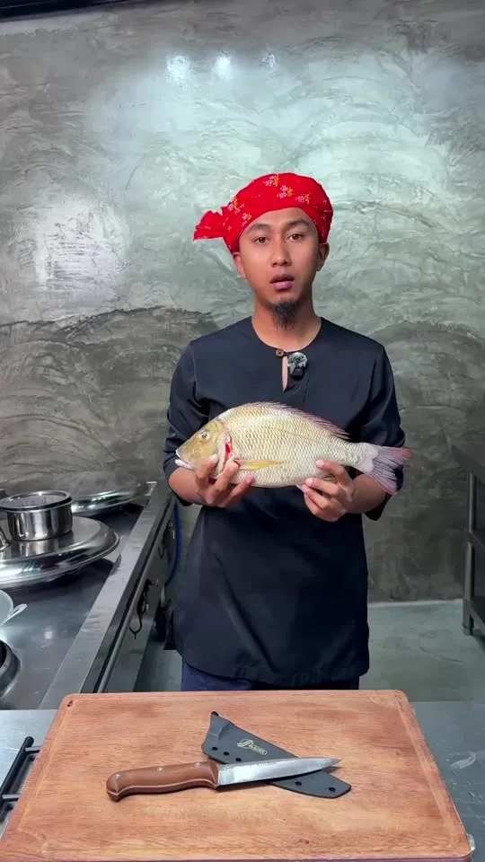 Abe Wea di dapur memegang ikan, dengan pisau FF Blades dan sarungnya di atas papan pemotong