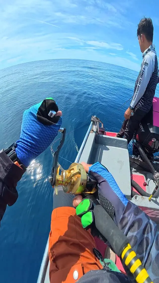 Tangan bersarung memutar reel jigging emas di atas bot di tengah laut