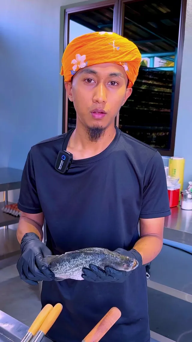 Abe Wea memegang seekor ikan siakap di dapur keluli