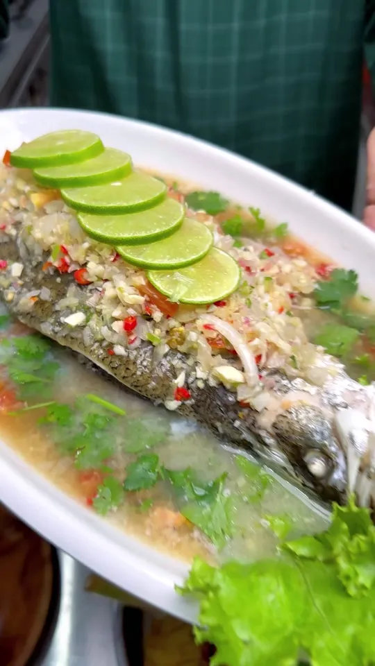 Ikan siakap stim dengan hirisan limau nipis, cili dan daun salad di atas pinggan bujur