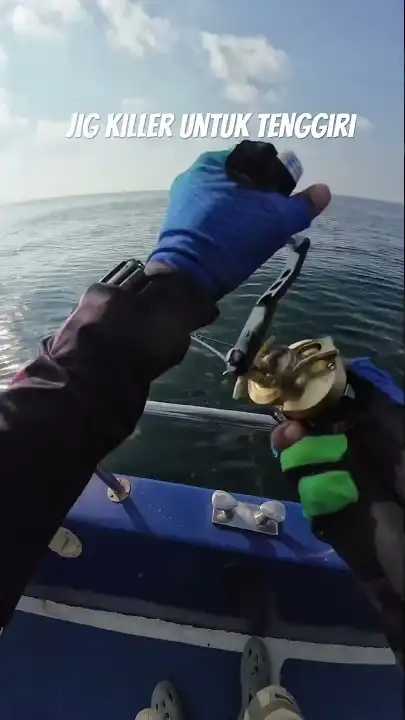 Tangan memegang joran dan reel jigging emas di atas bot di tengah laut