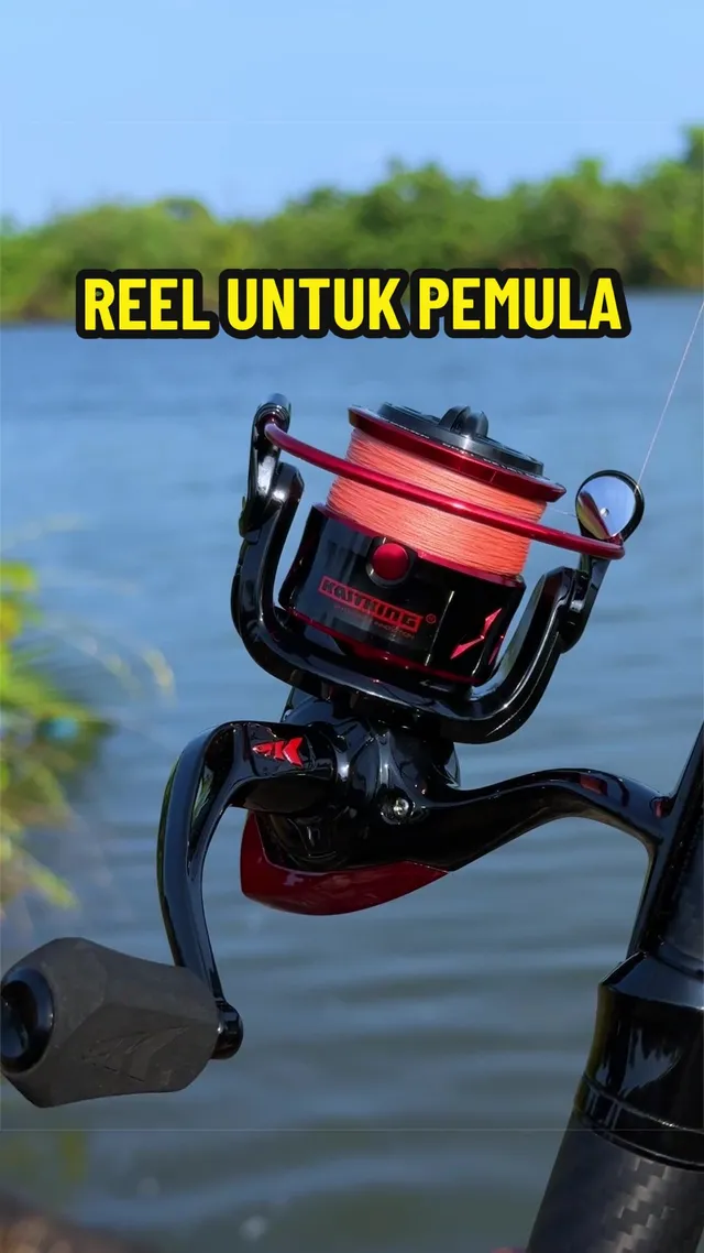 Reel spinning KastKing merah hitam pada joran, dengan air dan pokok di belakang