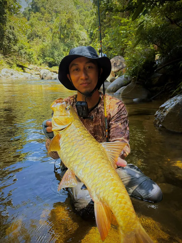 Abe Wea melutut dalam sungai jernih memegang ikan tengas besar