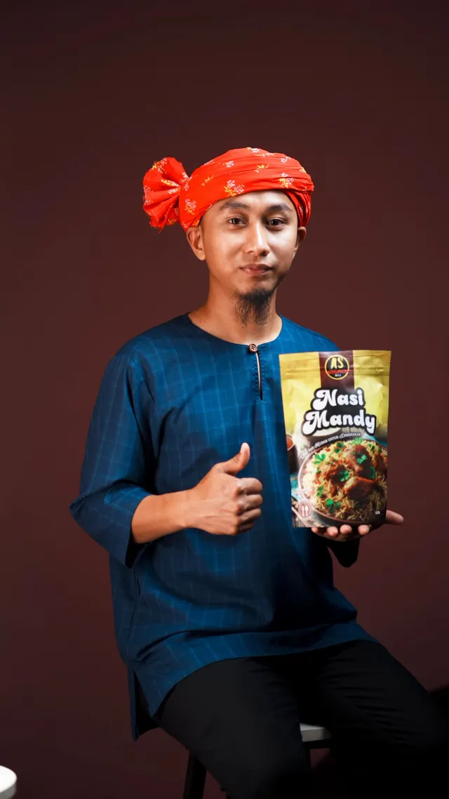 Abe Wea duduk memegang pek Nasi Mandy AS Kitchen sambil menunjukkan isyarat bagus