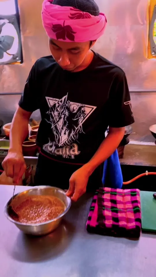 Abe Wea mengacau sambal belacan dalam mangkuk keluli di dapur