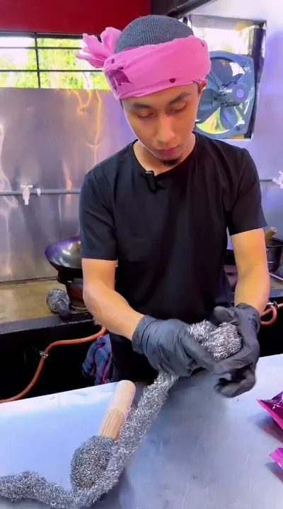 Abe Wea membuat berus kuali di meja keluli di dapur