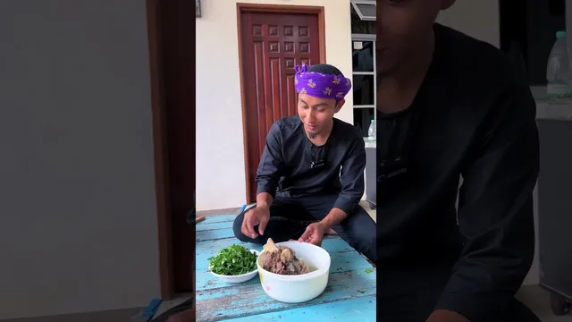 Abe Wea duduk bersila di atas pangkin kayu biru dengan semangkuk sup gear box dan semangkuk daun