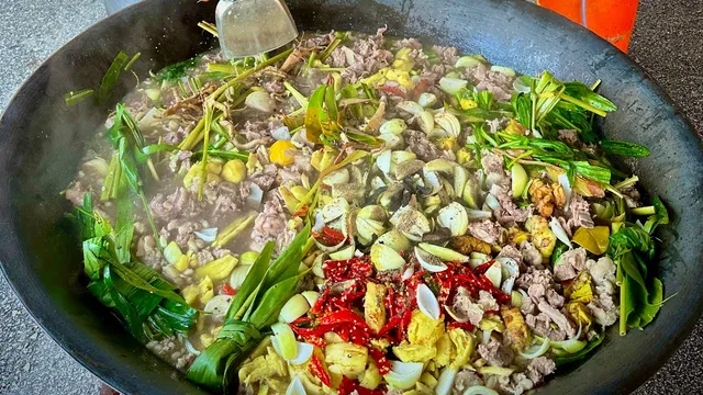 Kawah besar berisi daging, bawang, cili merah dan daun-daun, sedang berasap