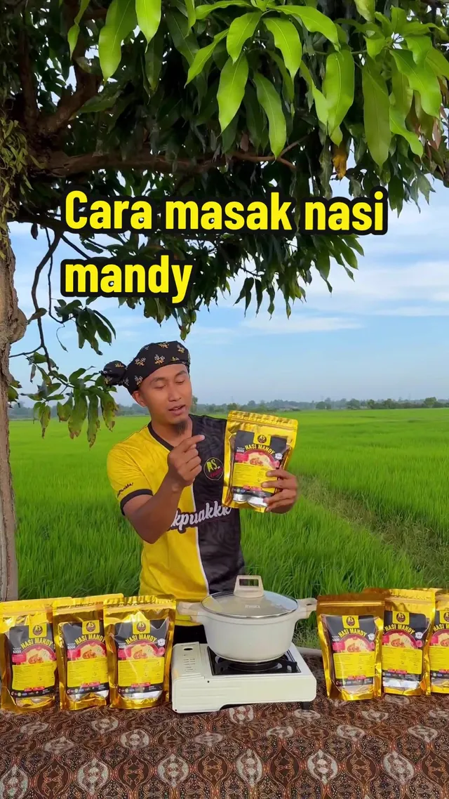 Abe Wea di sawah padi memegang pek Nasi Mandy AS Kitchen, dengan periuk nasi di atas meja