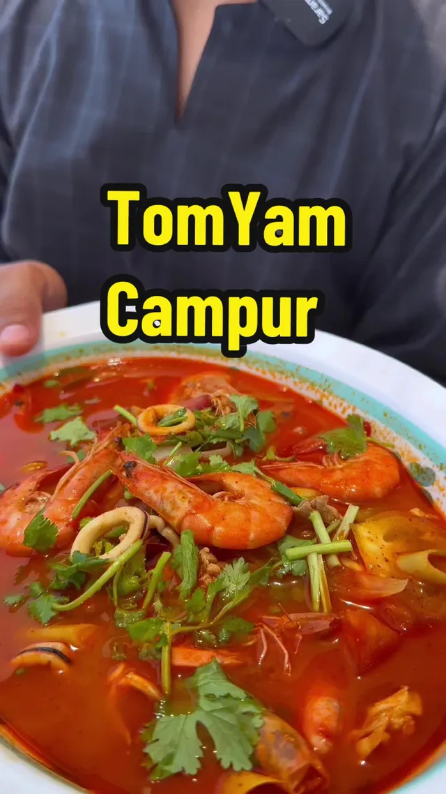 Semangkuk tomyam campur dengan udang, sotong dan daun ketumbar, dengan tulisan TomYam Campur