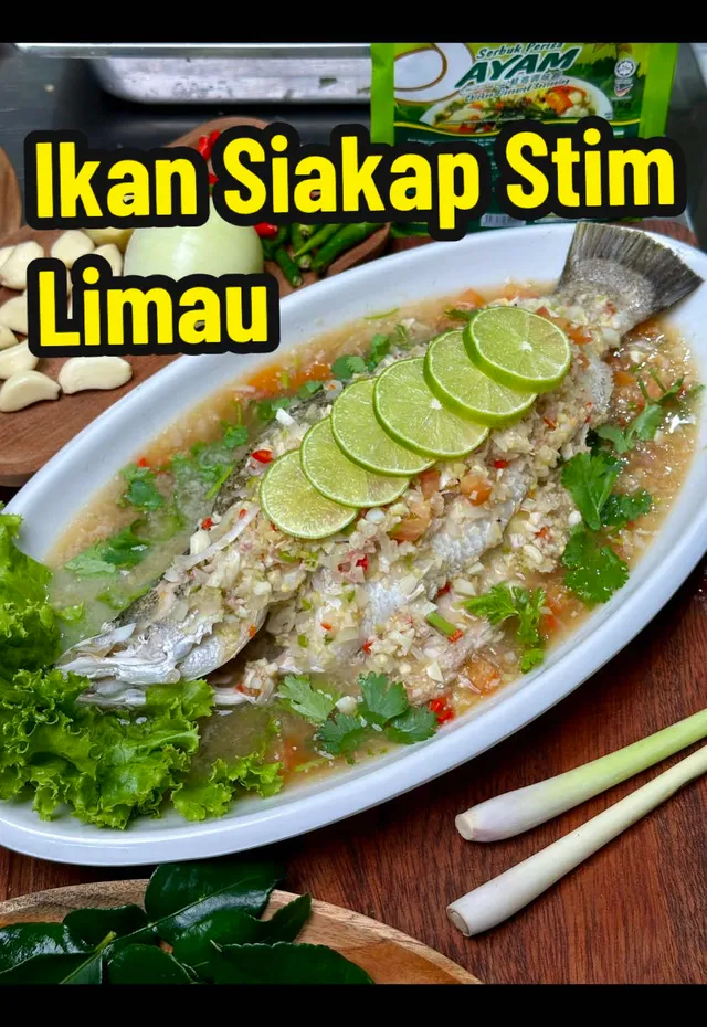 Ikan siakap stim limau di atas pinggan bujur dengan bahan masakan, dengan tulisan Ikan Siakap Stim Limau