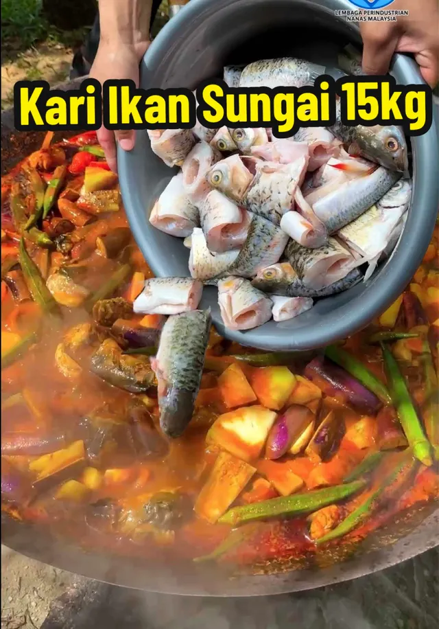 Ikan sungai dituang dari besen ke dalam kawah kari bernanas, dengan teks 'Kari Ikan Sungai 15kg'