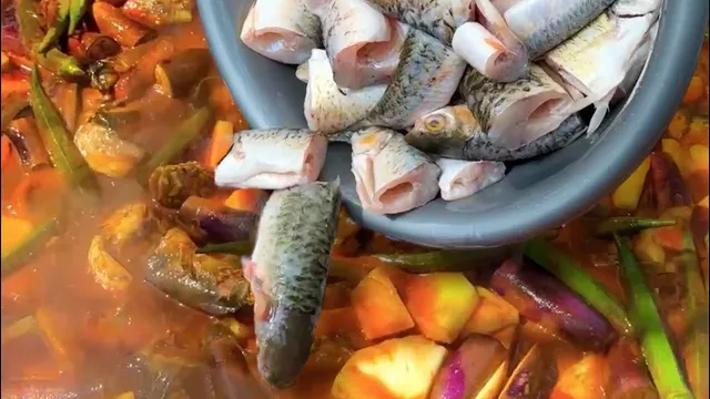 Potongan ikan sungai dituang dari besen ke dalam kawah kari dengan nanas, bendi dan terung