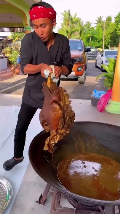 Abe Wea mengangkat kepala haiwan yang sudah dimasak dari kuali besar berkuah